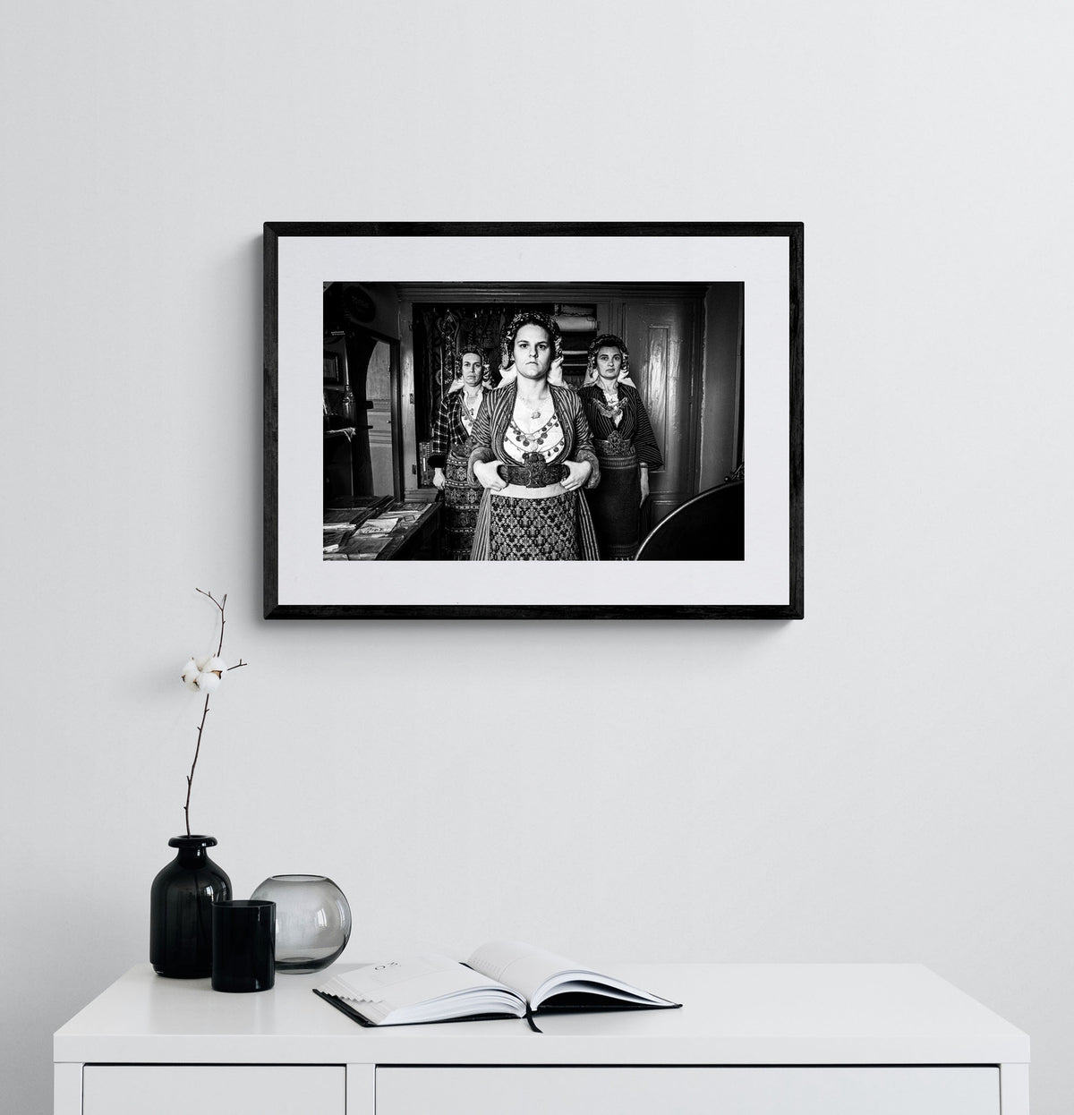 Black and white portrait of a woman in traditional attire with two other women in the background. Soufli local dresses, Thrace, Greece. Photography framed on a wall by George Tatakis