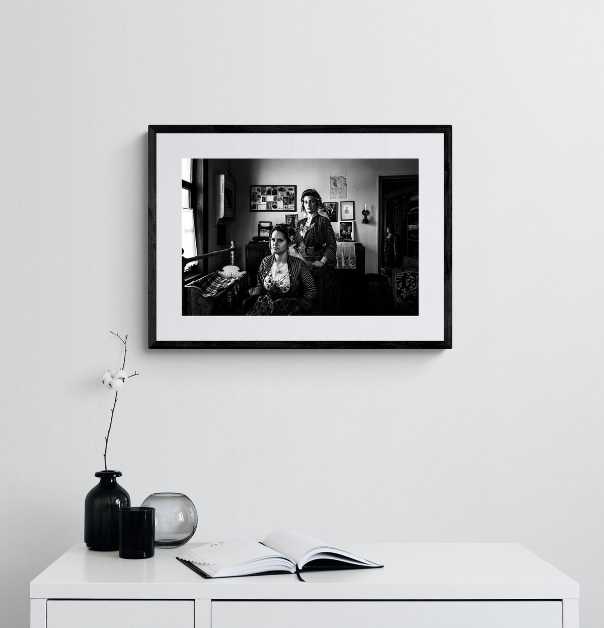 Two women in a room with framed pictures on the wall. Local dresses of Soufli, Thrace, Greece. Black and white photography framed on a wall by George Tatakis.